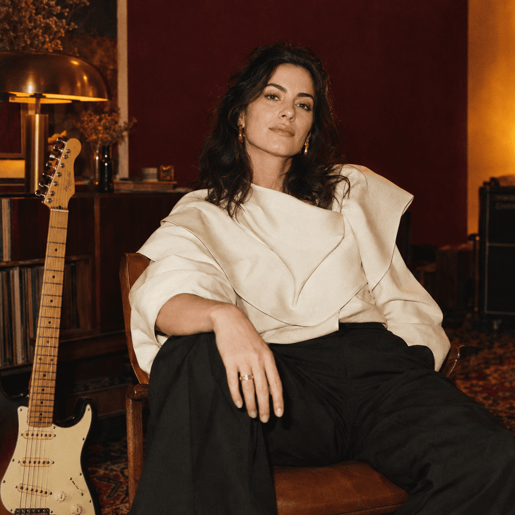 An adult creator in a warmly lit studio with a guitar beside her